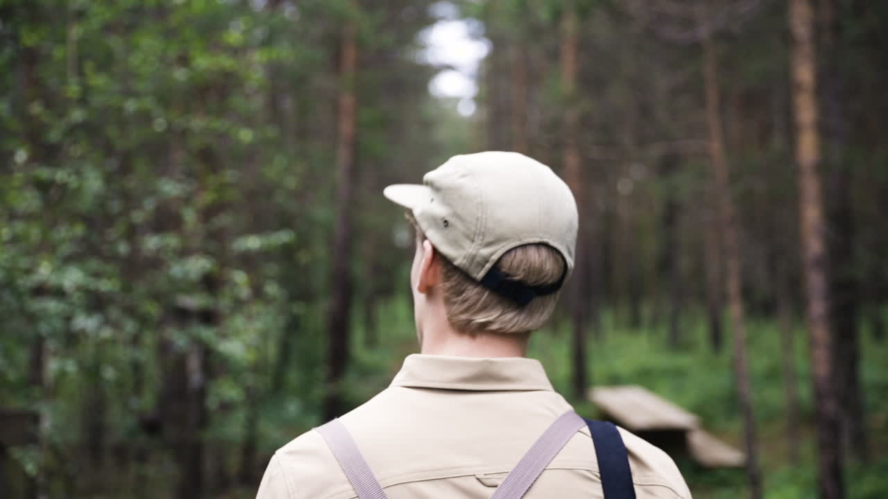 vista cercana desde atrás del hombre rubio con gorra caminando por el bosque