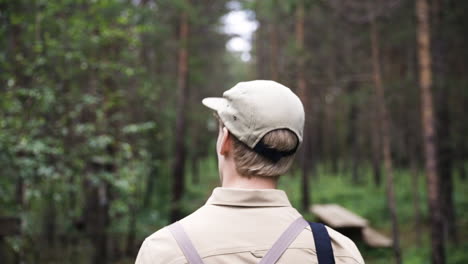 close view from behind of blonde man with cap walking through forest