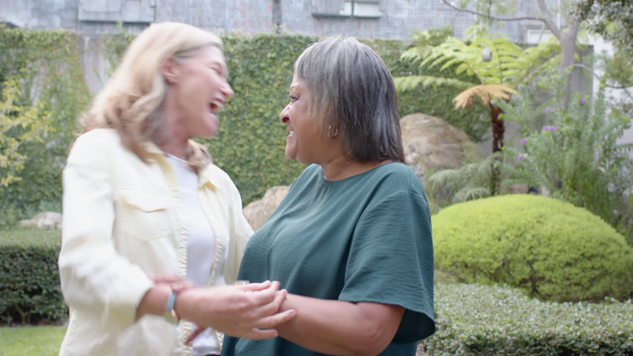 Smiling multiracial senior female friends enjoying conversation and bonding in garden setting