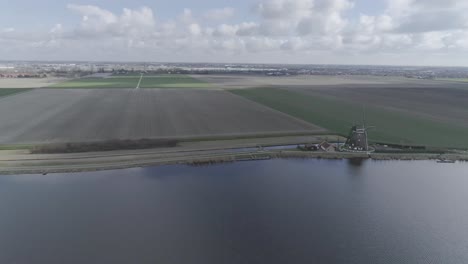 Toma-De-Drones-En-Movimiento-Rápido-De-Tierras-De-Cultivo-Holandesas-Con-Molinos-De-Viento-Y-Río