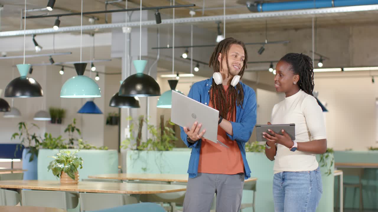 Afroamerikansk team sjekker nettbrett og laptop, mann peker, kvinne scroller og nikker bekreftende på kontoret