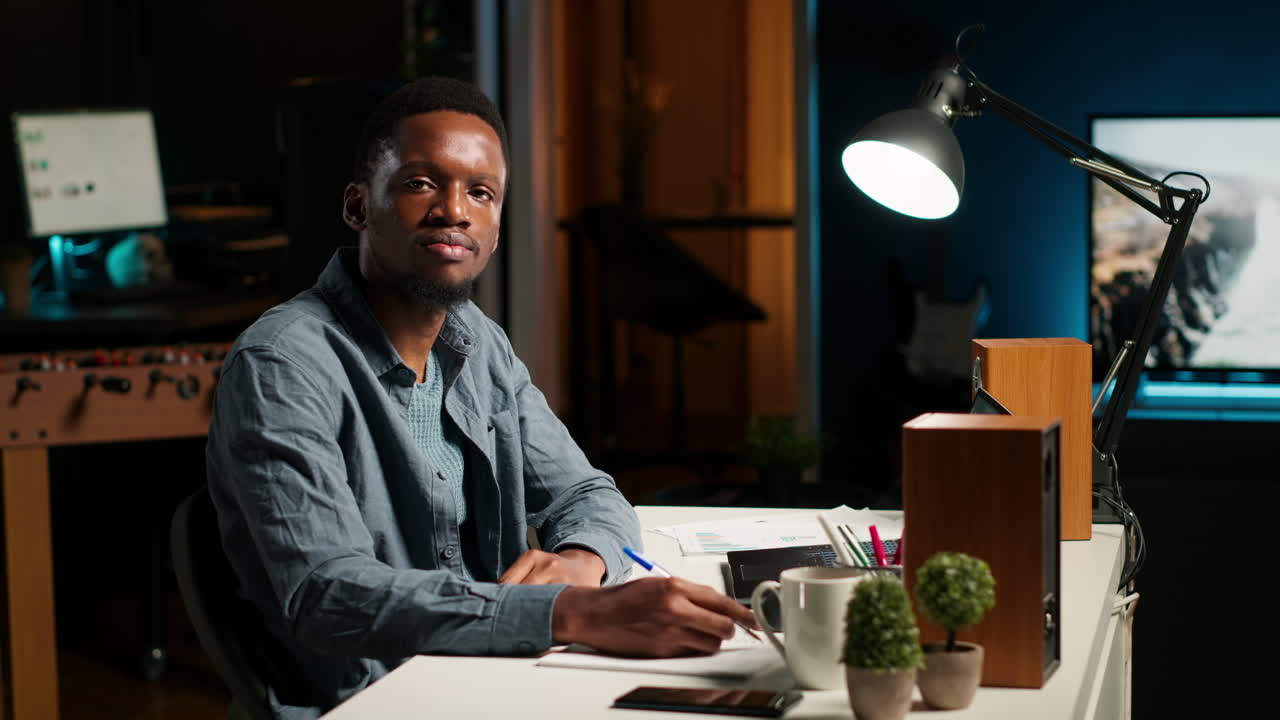 Black man participates in online video call meeting waving from his office