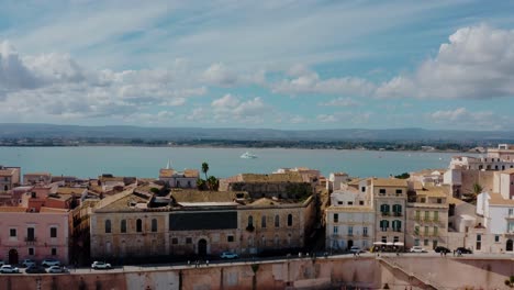 aerial view of ortigia island. flying above medieval old town buildings by mediterranean sea with yacht in a distance. unesco world heritage site in syracuse, sicily.