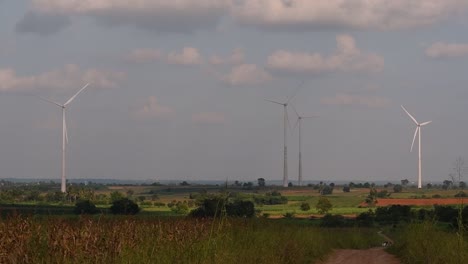 wind turbines towering farmlands, as farmers grow their crops and tend their animals; clean alternative energy in thailand and mainland southeast asia.