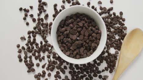 Video-of-overhead-of-bowl-of-chocolate-chip-with-wooden-spoon-over-white-background