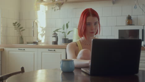 beautiful girl typing message on laptop at table in sunlit kitchen