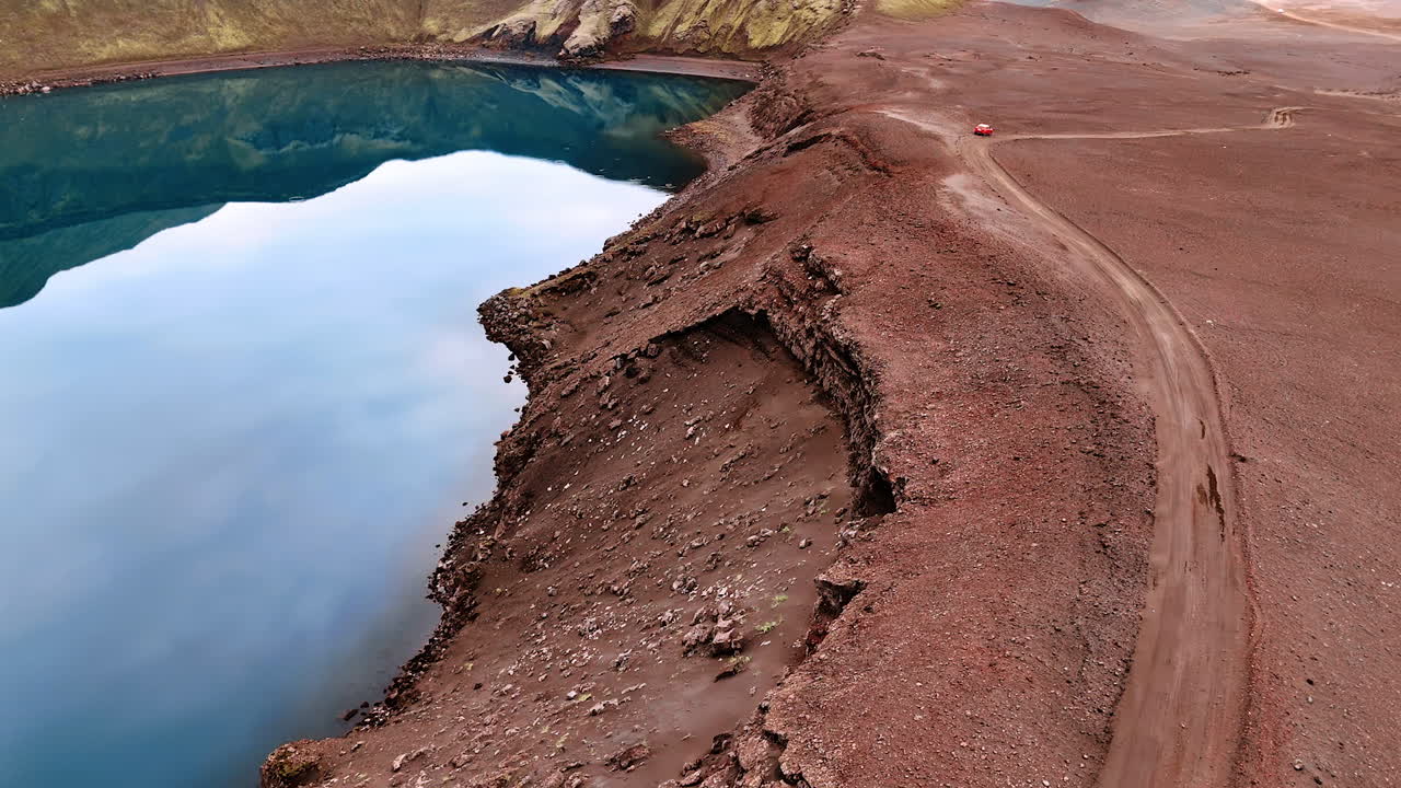 Flight above the road on the hill above the lake. Crater of a sleeping volcano filled with water. Iceland nature.