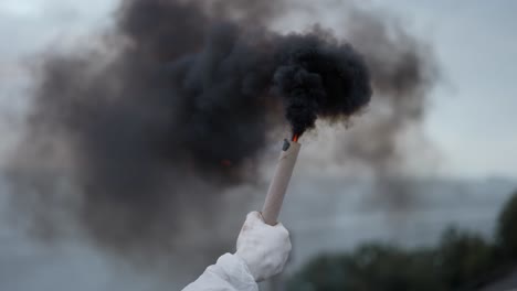 man in protection suit on his knees on the roof with black smoke stick