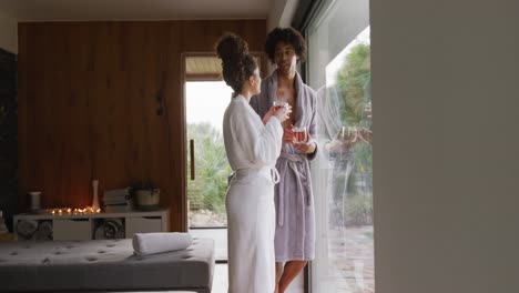 video of relaxed diverse couple in bath robes drinking tea and talking at health spa