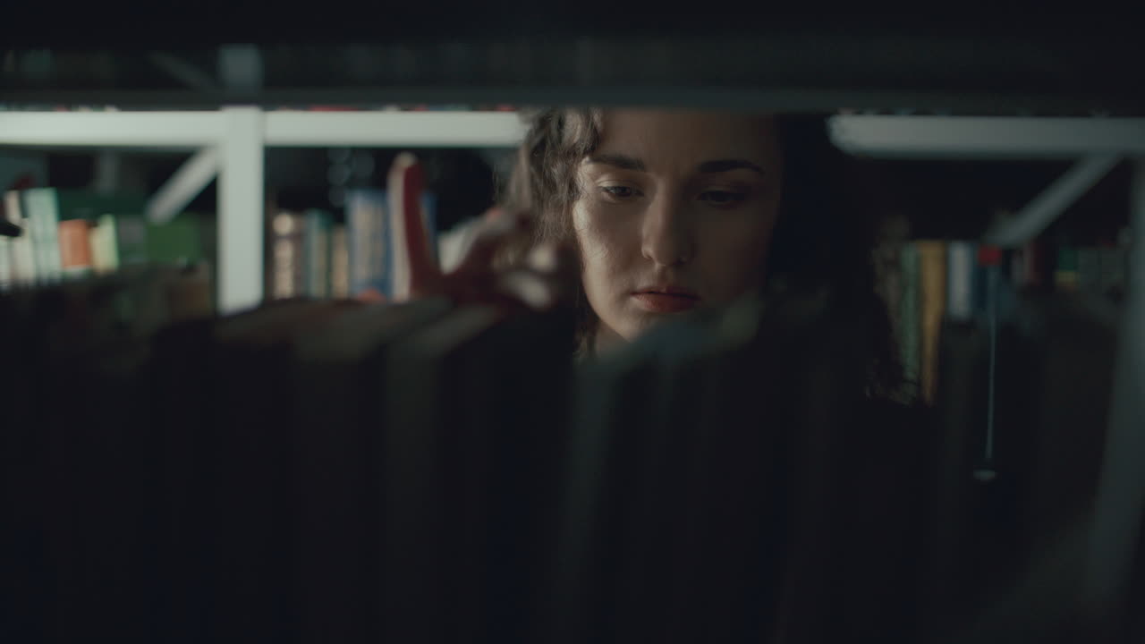 Young Woman Searching for Specific Literature on Bookshelf in Library