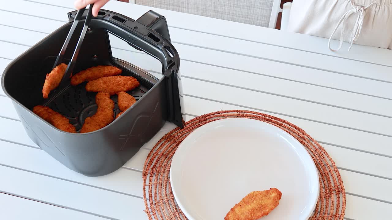 Chicken tenders are removed from an air fryer and placed onto a plate in a bright kitchen setting