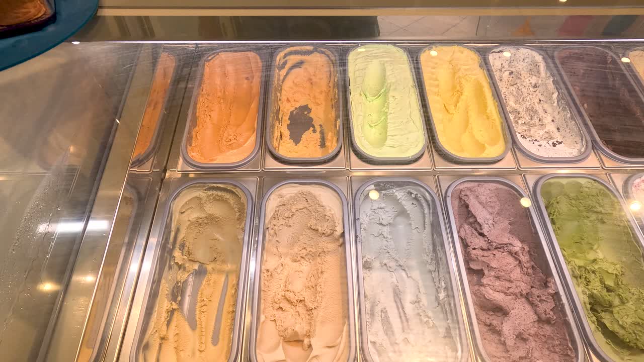 Overhead view of assorted gelato flavors in a well-lit dessert shop display counter