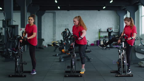 healthy caucasian group of women exercising workout on stationary cycling machine bike in gym