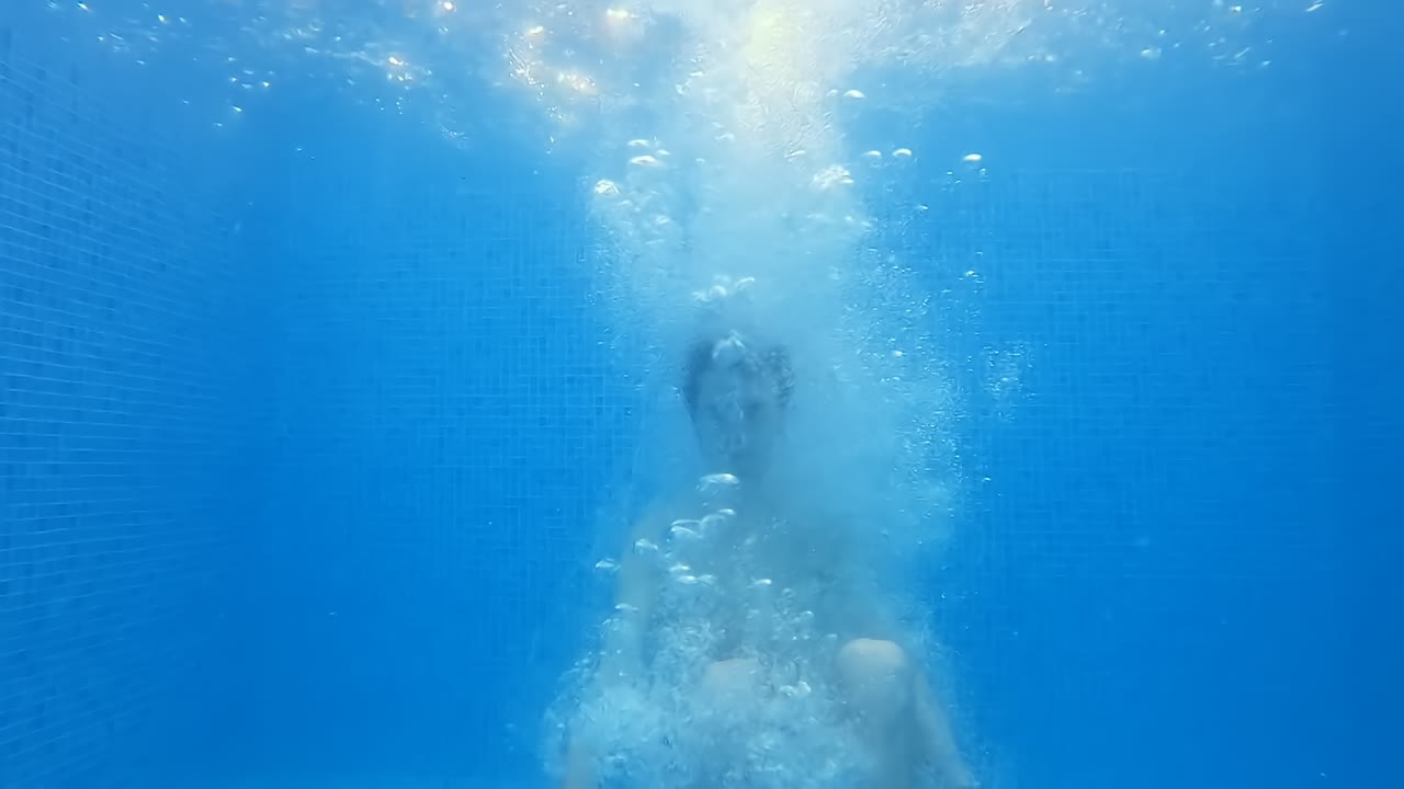 Tall young man jumping into the pool. Slow motion. Underwater view