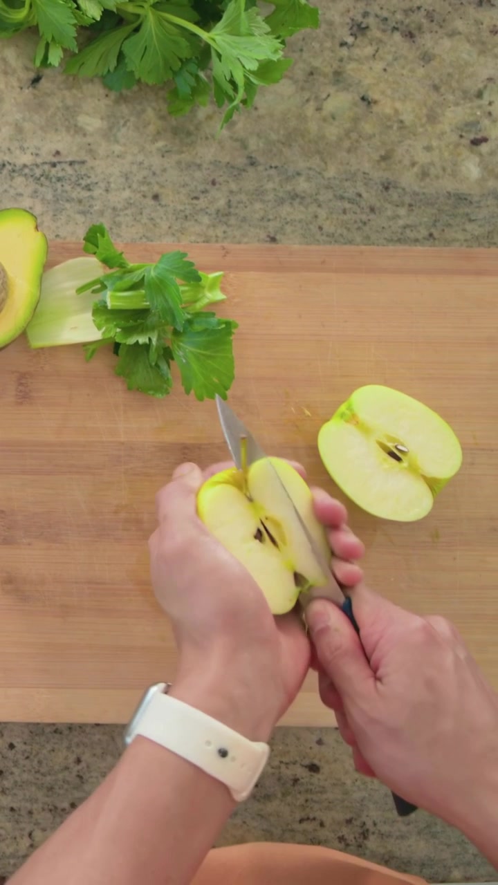 Video verticale: Cuoco casalingo che posiziona una mela verde e taglia il torsolo con un coltello in spicchi per la preparazione dei pasti.