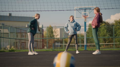 tres mujeres en leggings y capuchones participan en una actividad de fitness en un patio al aire libre con un edificio residencial y árboles en el fondo, mostrando trabajo en equipo y movimiento
