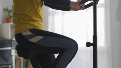 Entrenamiento-Con-Bicicleta-Estacionaria-En-Casa-La-Mujer-Gira-Los-Pedales-Manteniéndose-En-Forma-Y-Perdiendo-Peso-Detalles-Del-Cuerpo-Femenino-Delgado-Filmados