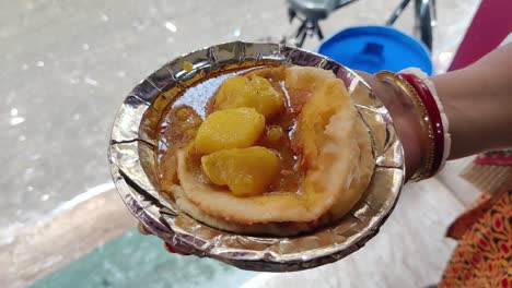 close up shot of female hands holding a platter of several pooris and spicy masala aloo dum from a roadside stall