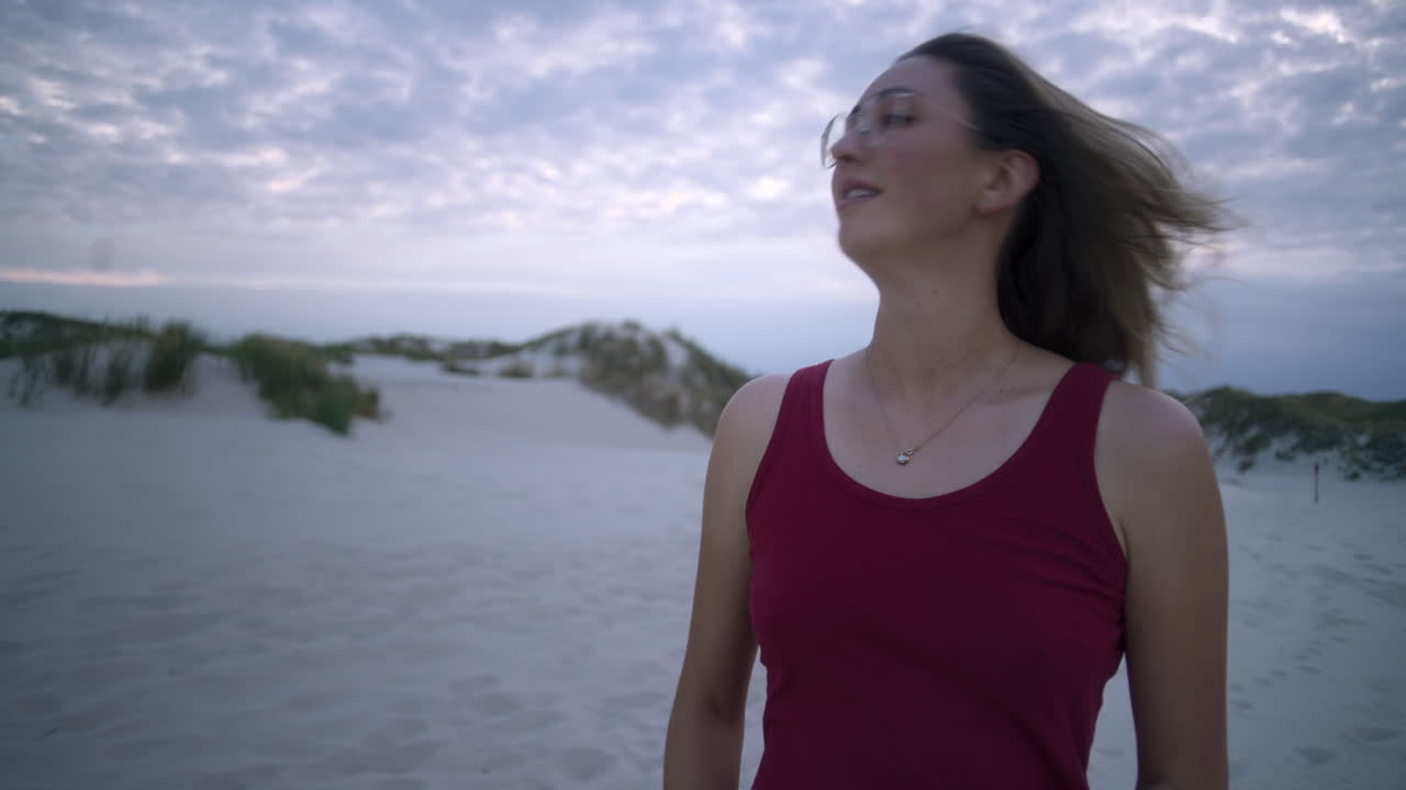mujer joven en vestido rojo abre su cabello en una playa blanca