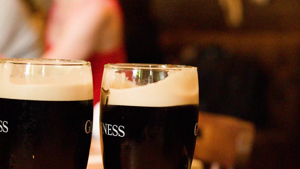 Hand grabs dark stout pint on wooden table in warmly lit pub interior
