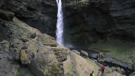 dos personas caminando por un cañón cubierto de musgo verde en islandia hasta la cascada kvernufoss