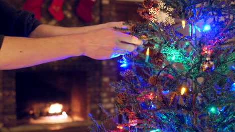 Close-up-on-a-family-decorating-a-christmas-tree-together-with-lights-and-ornaments-and-stockings-over-the-fireplace-during-the-holidays