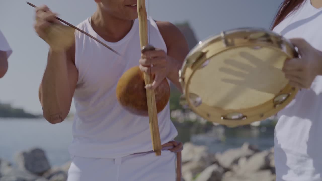 Capoeira musicians playing traditional Brazilian instruments by the water