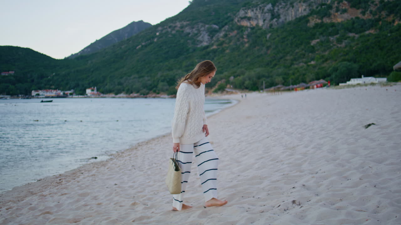Traveler walking sand shoreline holding bag. Relaxed woman enjoying beach