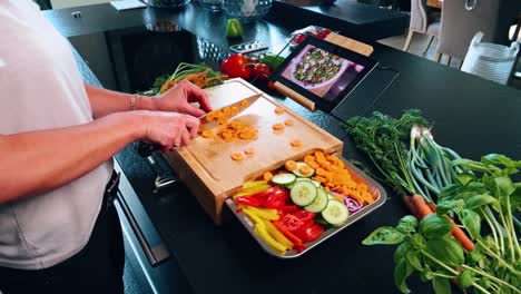 tabla de cortar con cuchillo y zanahoria con otras verduras y una tableta con recetas