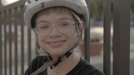 a cute kid with a bike helmet and glasses outside smiles at camera