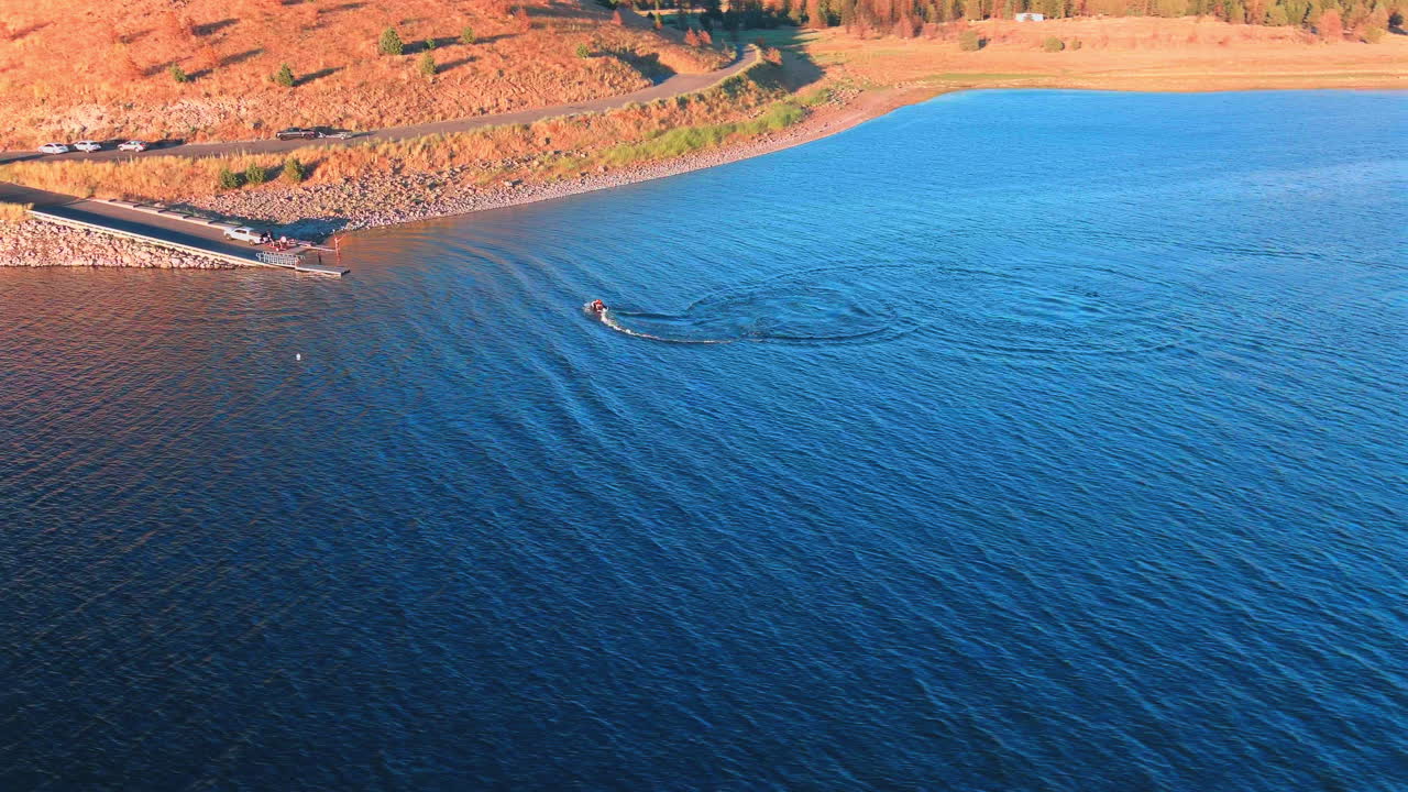 Aerial view of a jet ski making circles on a lake near a boat ramp