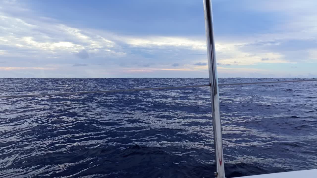 Ocean waves shimmer under soft sunset light seen from deck of a sailing yacht