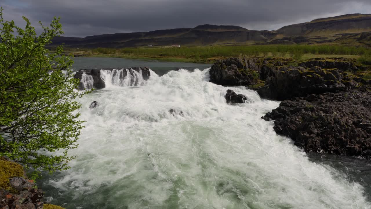 movimiento lento de una cascada tranquila que fluye sobre las rocas con montañas y nubes en el horizonte