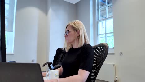 a woman, an office worker, seated in a professional business environment, focuses on her computer screen, embodying the concept of productivity and dedication in the workplace