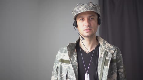 military-man-in-headphones-talking-in-slow-motion-looking-at-camera.-Video-chat-POV-portrait-of-brave-male-soldier-conferencing-online-standing-indoors