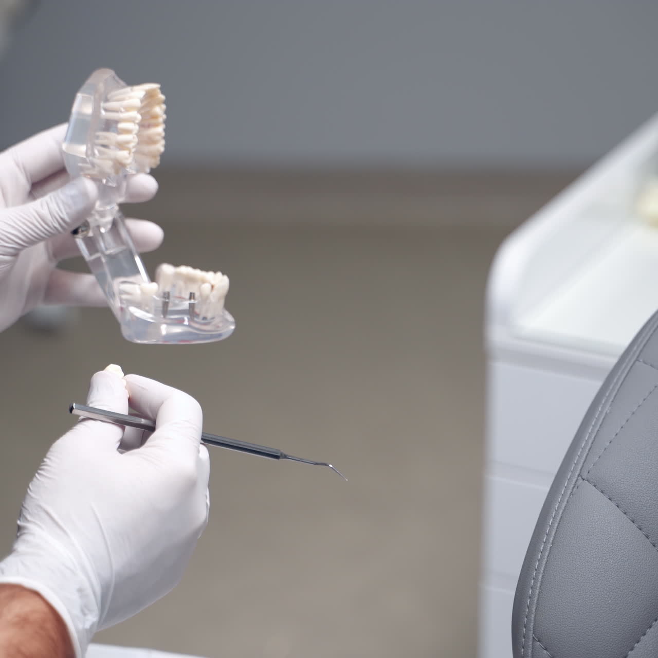 Doctor's hands hold plastic jaw model. Dentist shows artificial teeth to a female patient in stomatology office. Close-up. Dentistry.