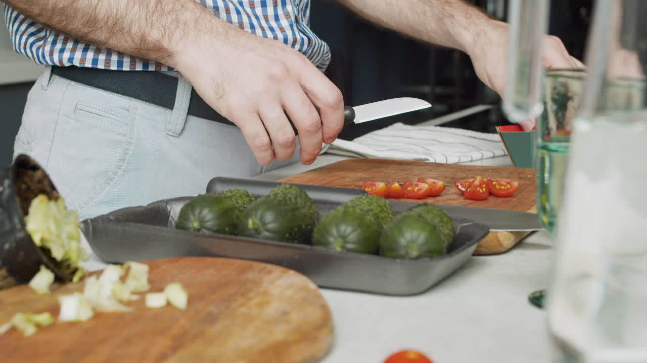 primer plano de las manos de un hombre cortando tomates en una tabla de cortar de madera en una cocina moderna