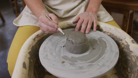 mid section of female potter using loop tool for finishing pottery at pottery studio