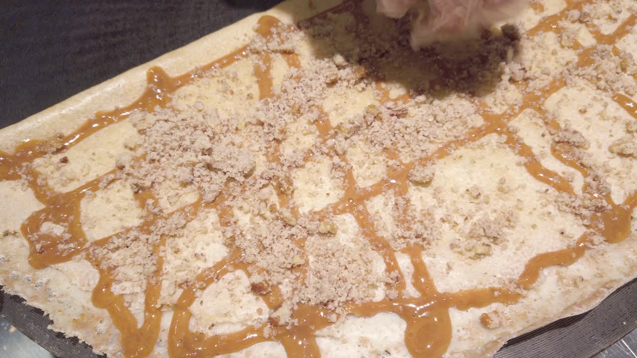 Sweet caramel and crushed nuts being sprinkled on a freshly cooked crepe with zoom in on delicious topping details.