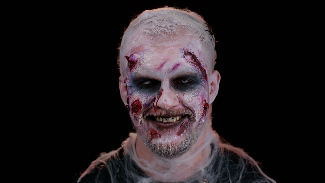 Playful sinister man Halloween crazy zombie with bloody wounded scars face blinking eye toothy smile