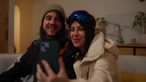 couple taking a selfie indoors, wearing winter gear.