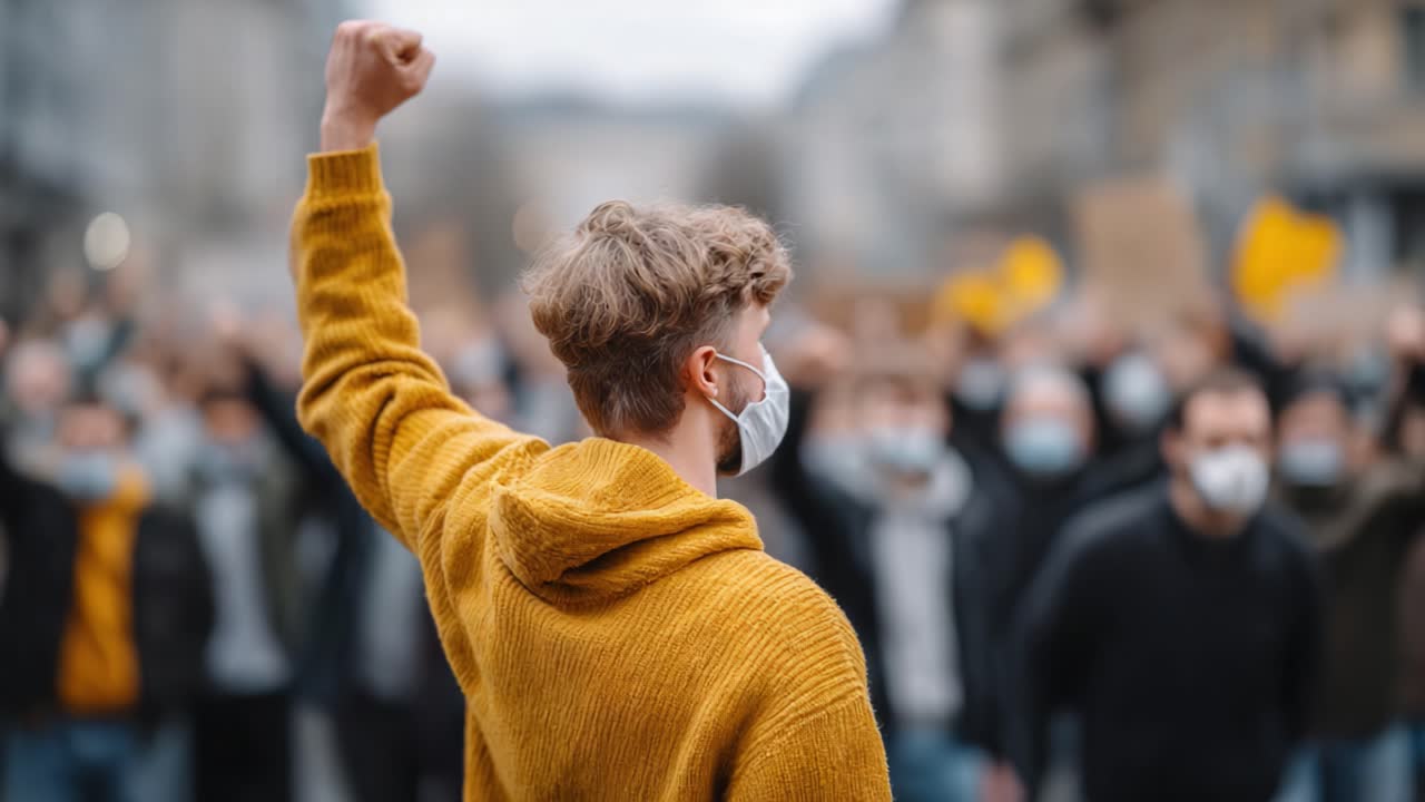 A passionate young individual raises a fist during a protest, symbolizing solidarity and strength among the crowd of demonstrators wearing masks in a unified stance