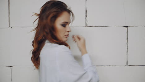 woman in a blue striped shirt posing in front of a white brick wall