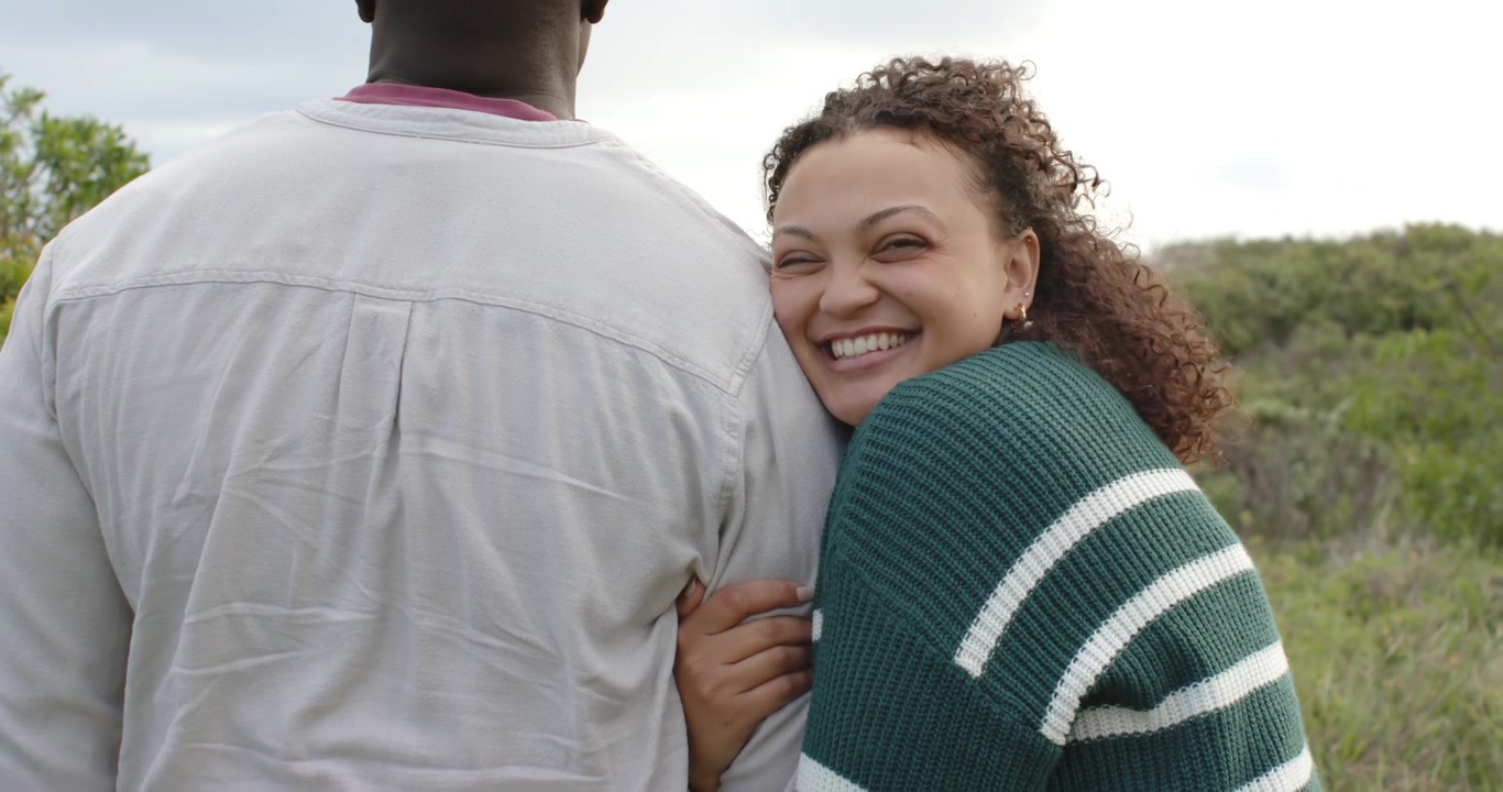 African American couple on dune wind lifting curls woman in sweater fixing hair leaning for comfort