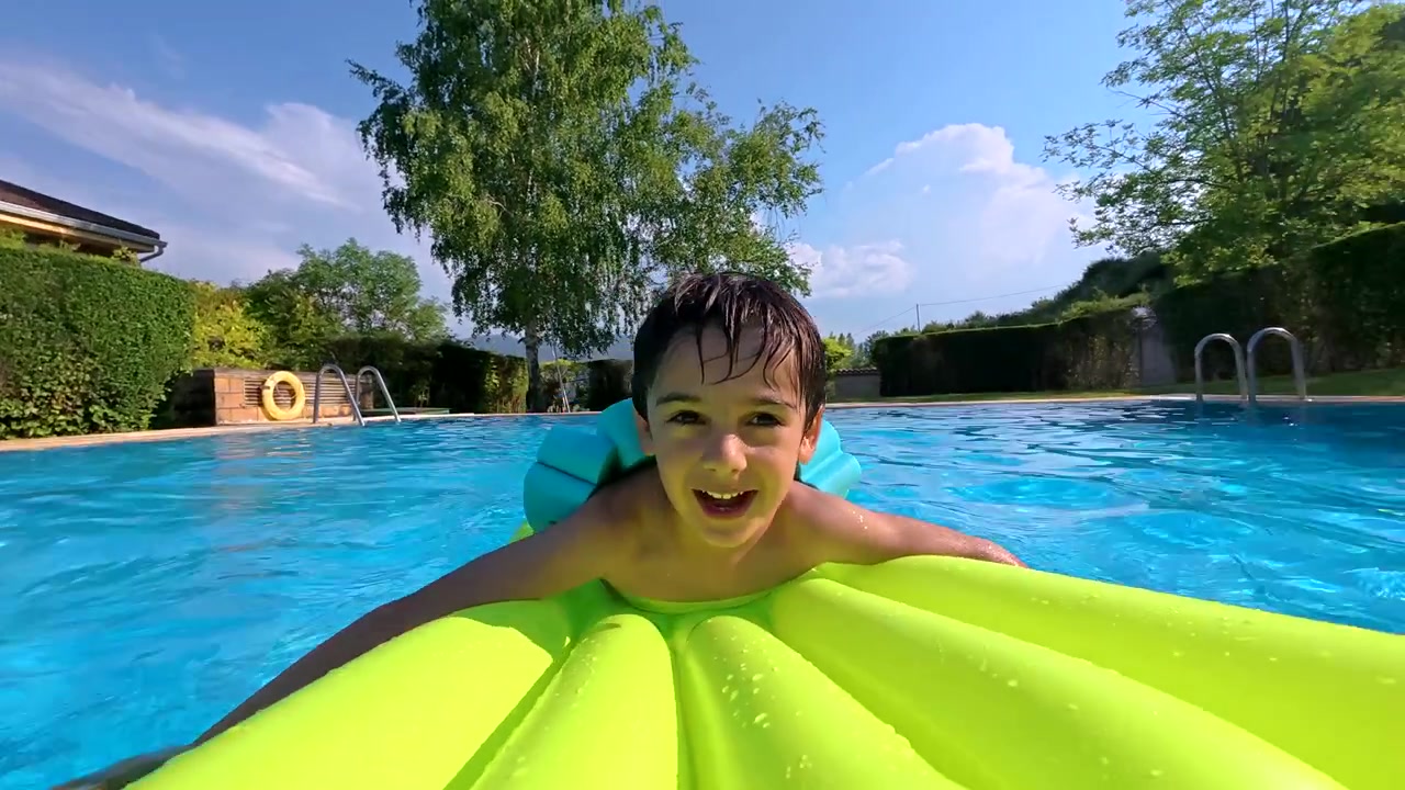 Happy Boy Floating on Inflatable Mattress in Swimming Pool