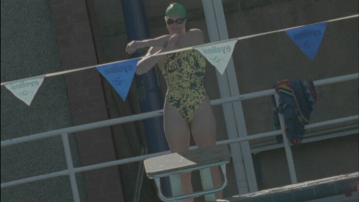 A young woman stretches stands up on the platform dives into the pool and starts swimming
