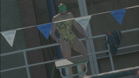 una joven se estira, se para en la plataforma, se sumerge en la piscina y comienza a nadar