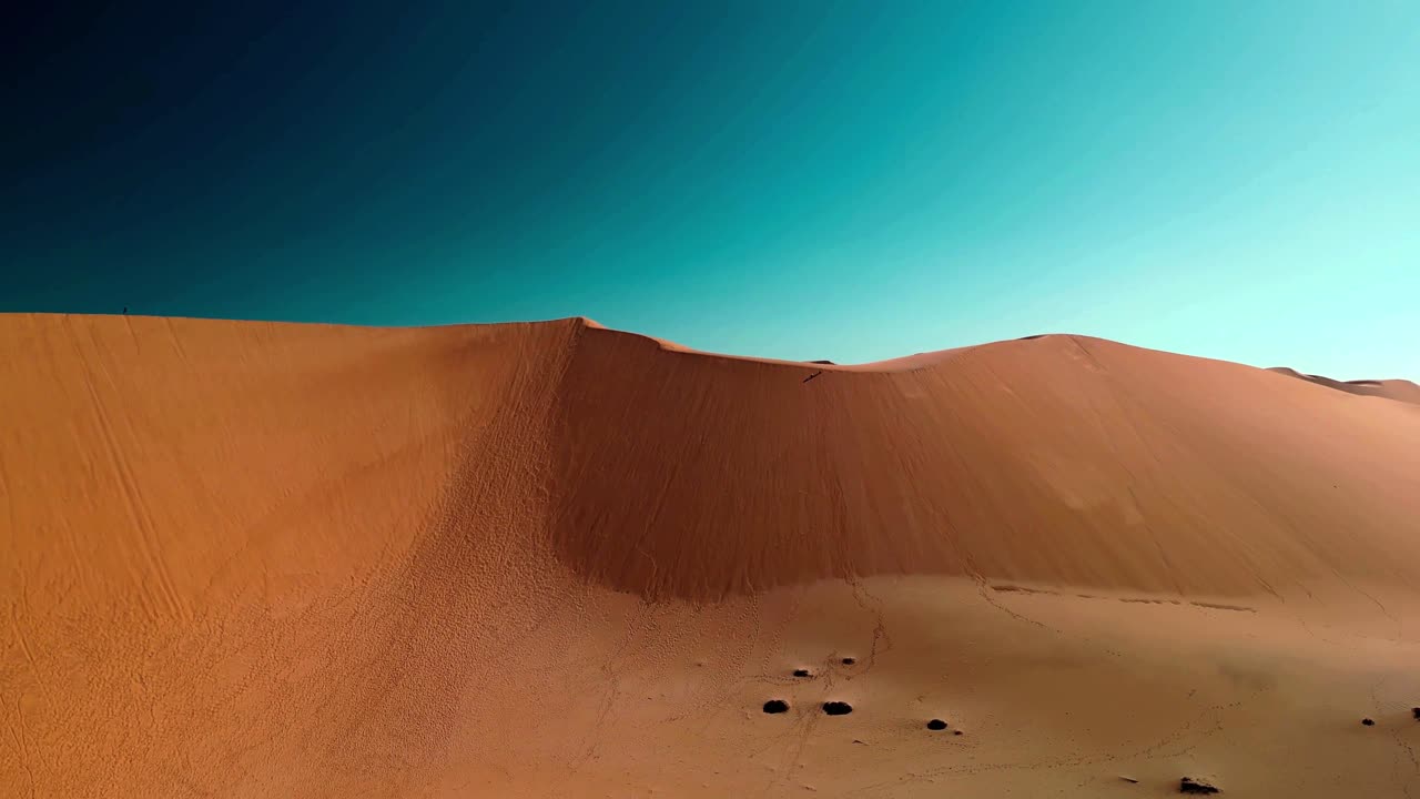 Aerial over towering desert sand dunes under a clear blue sky