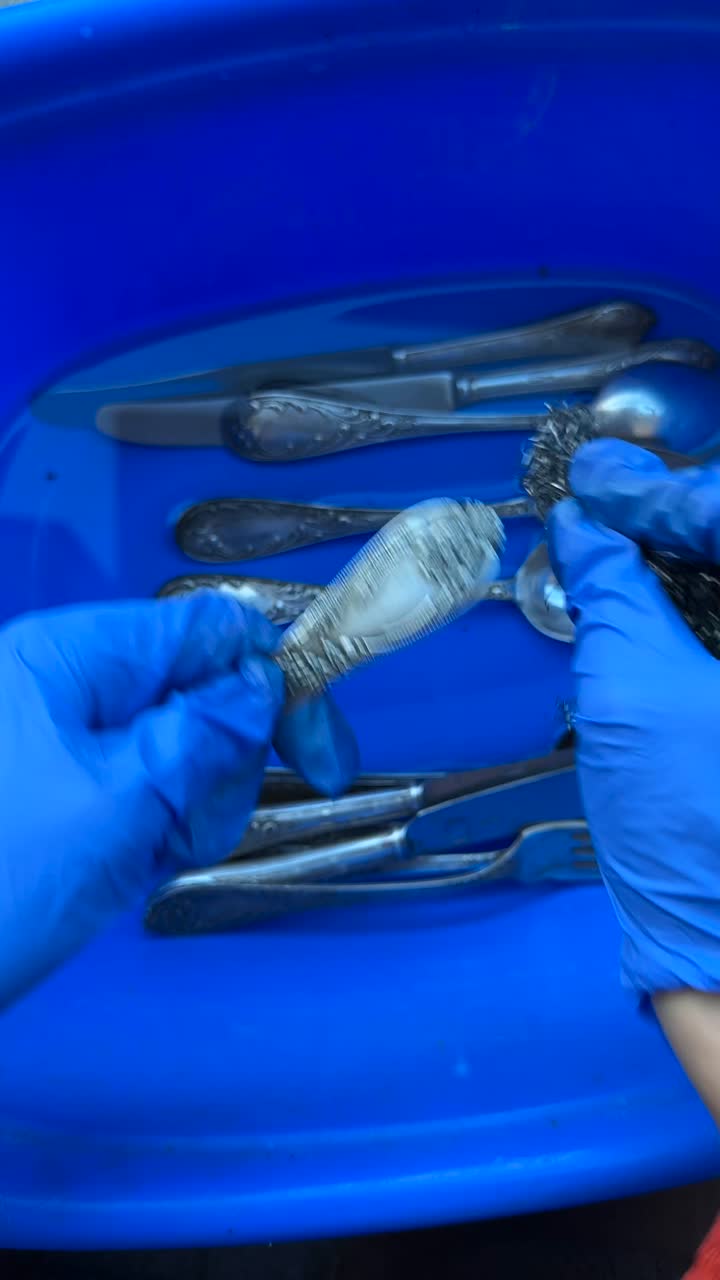Cleaning silverware with gloves in a blue plastic container