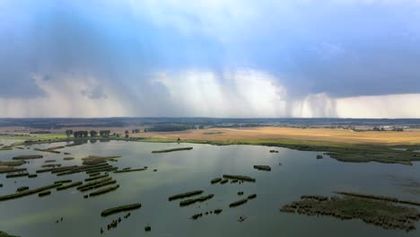 Toma-De-Elevación-Aérea-De-Humedales-Y-Vasto-Campo-Agrícola-Con-Tormenta-Distante